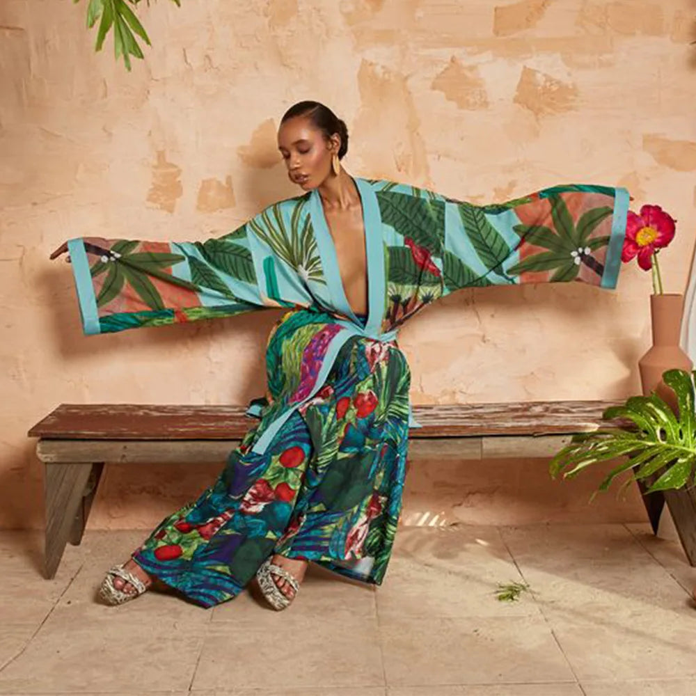 Woman wearing green tropical floral kimono with blue trim, arms outstretched on a bench